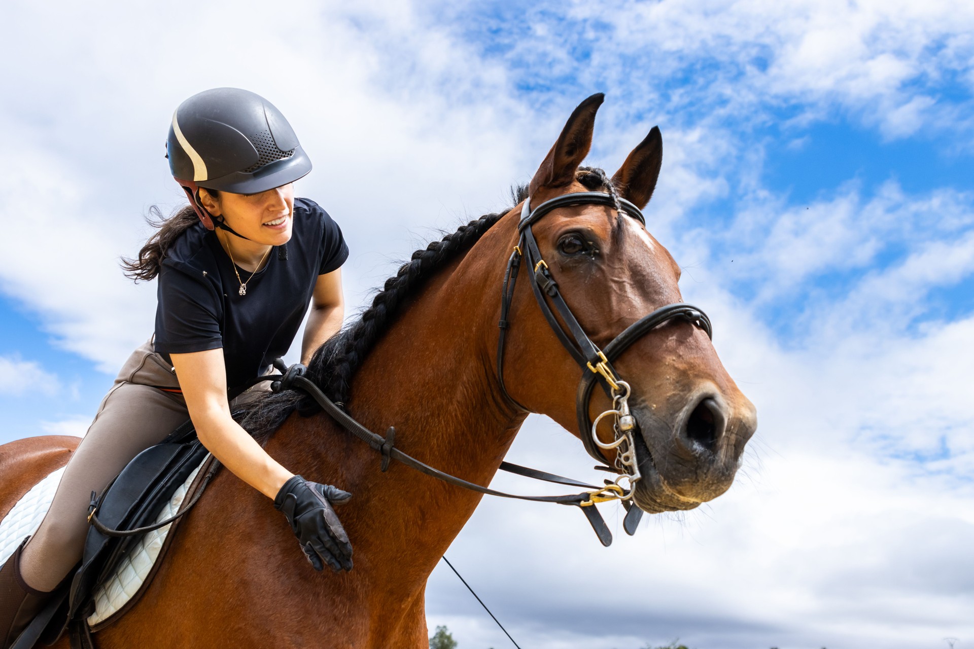 Young woman riding a horse and petting it under a cloudy sky